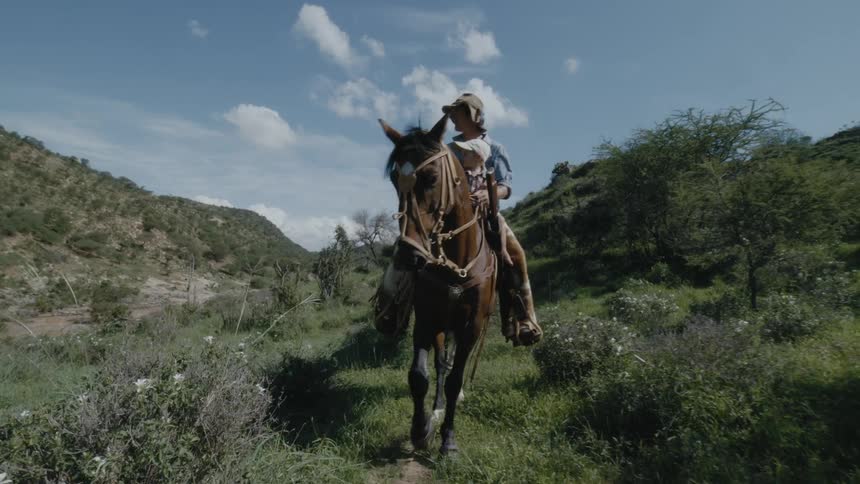 A man rides a horse with his toddler son on a trip through rolling hills