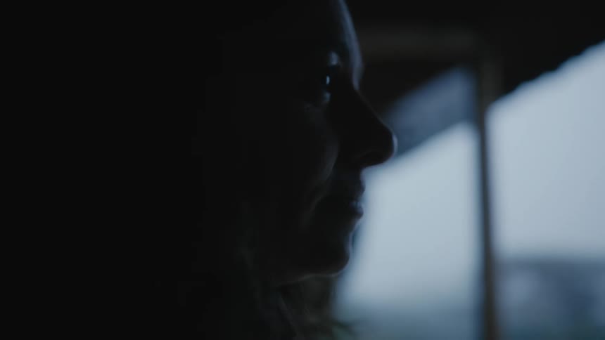A woman is looking out the window in the dark room