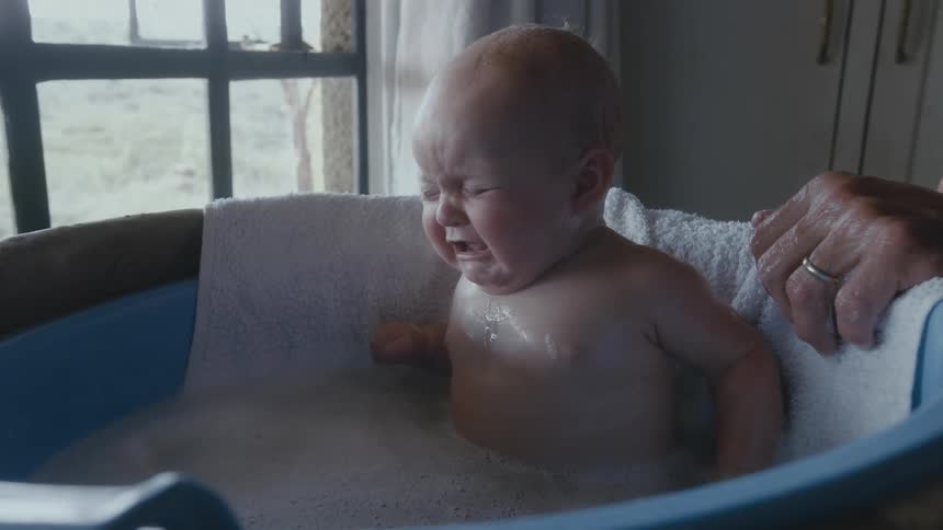 Man bathing a baby in a plastic tub next to the window