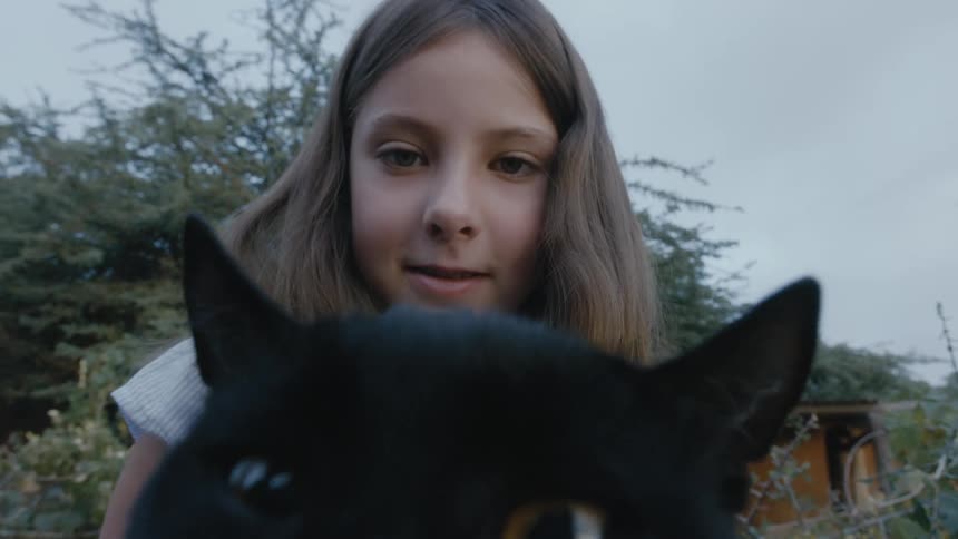 Girl with brown hair and white blouse holds black cat in the garden