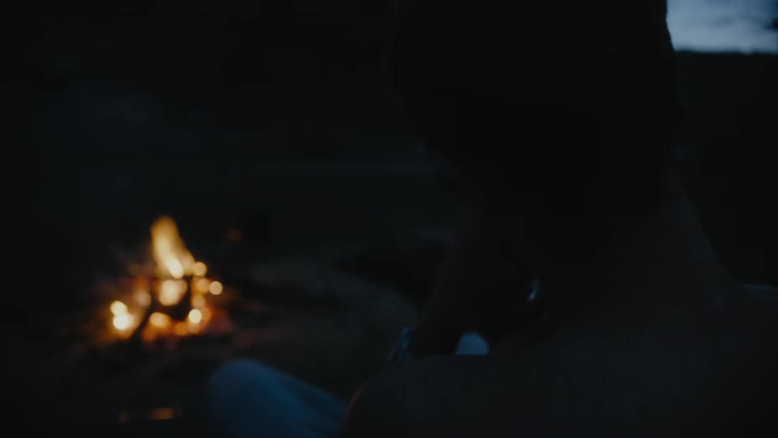 Man sits outdoors near burning campfire
