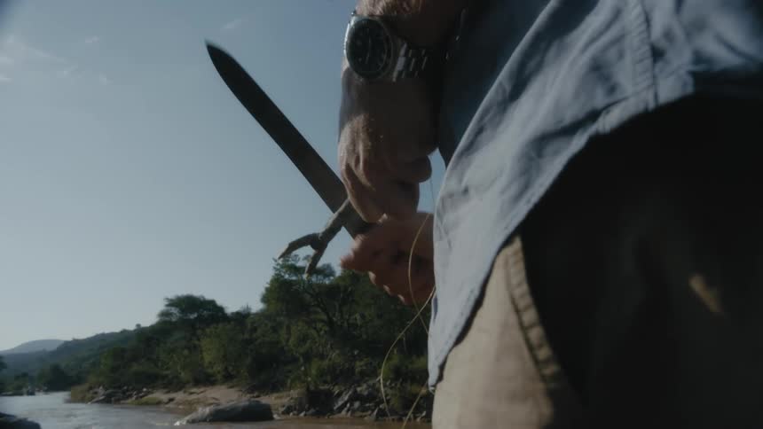 A man uses a long blade to shave down a tree branch