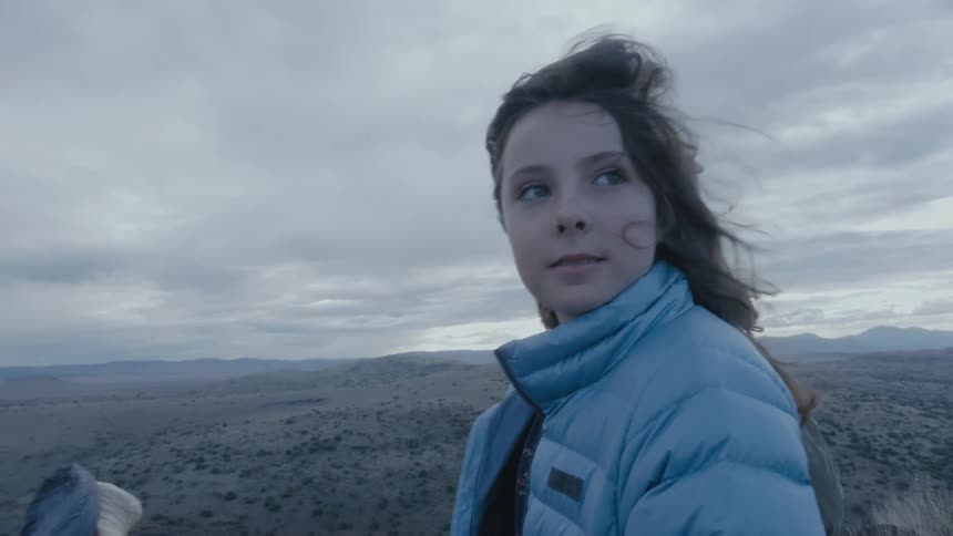 A young girl standing on a hilltop looking around at the view