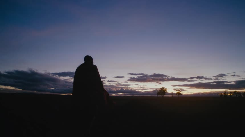 Man in a robe walks down a rural road at night