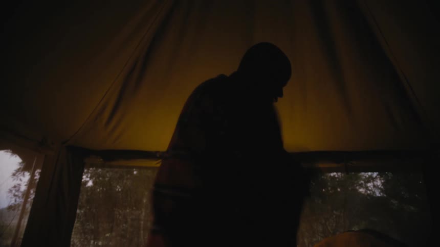 A man puts on a jacket and scarf and while standing in his yurt