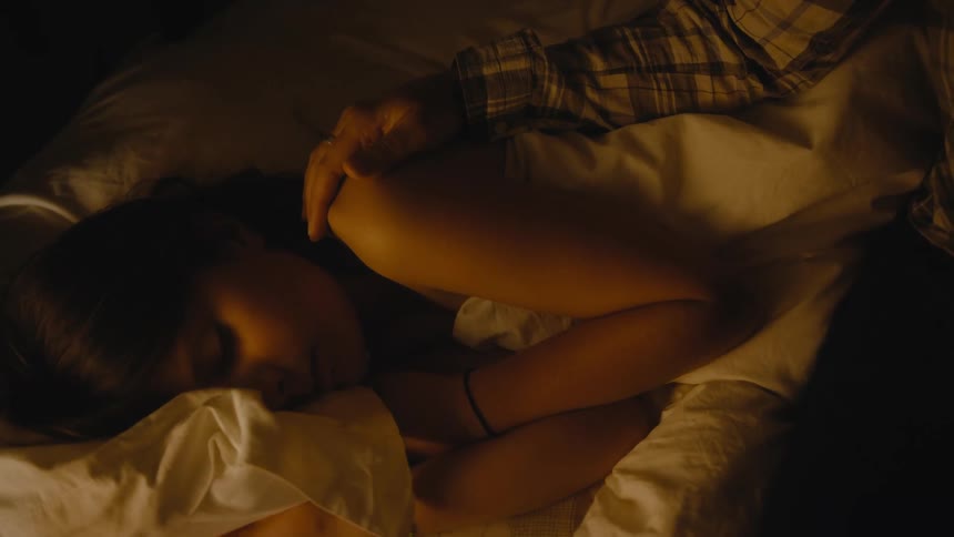 Mother sitting next to her daughter caressing her shoulder while shes sleeping in her bed