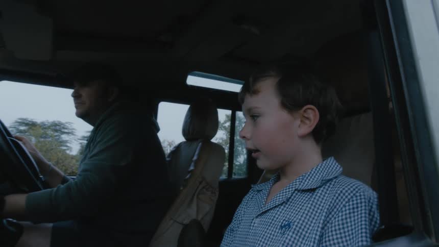 A young boy sits in a truck next to his dad as he starts it