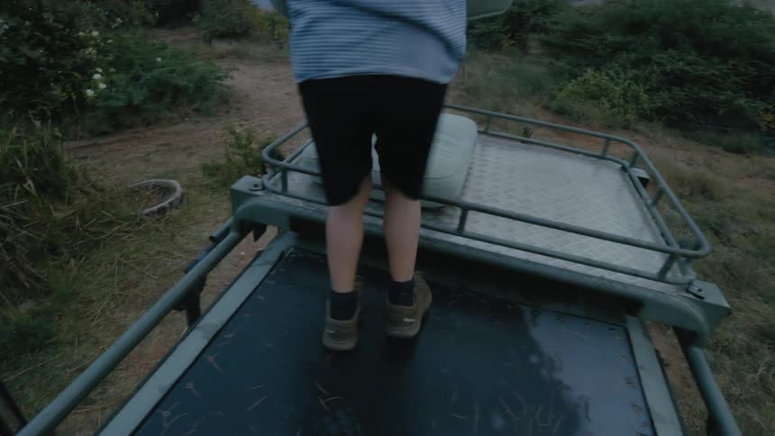 Girl throwing a cushion to his brother that is standing on top of a jeep