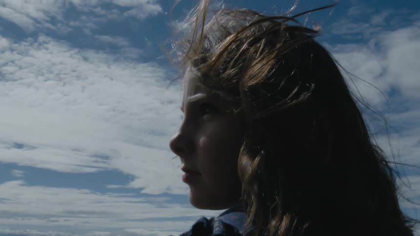 A teenager stands outside as the wind blows her hair around