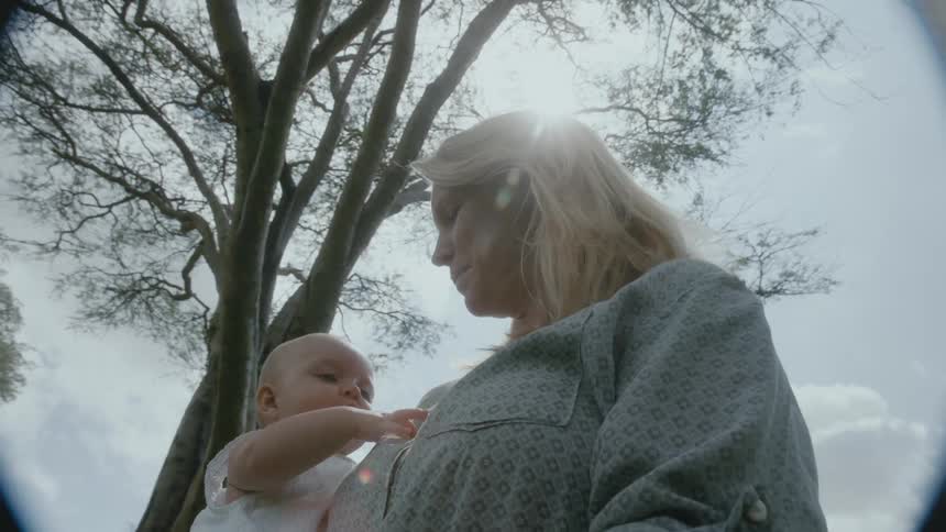 Mother holding her baby daughter while standing outdoors next to a big tree with the father on their side