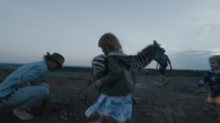 Children run towards mom who is squatting down near a baby zebra holding a stone