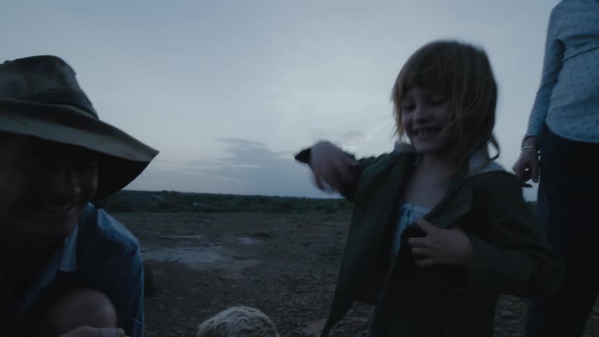 Father kneeling on the ground near a black dog shows his son and daughter a small scorpion