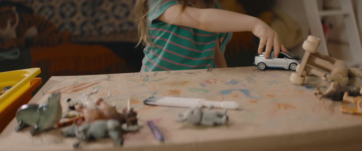 Little girl wearing a t-shirt sits at a table and plays with a toy car