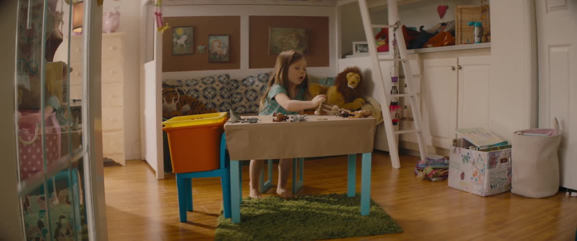 A young girl coloring at a small table stops to play with a wooden horse