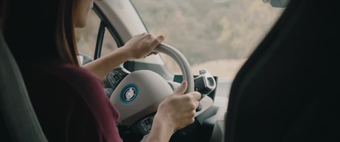A woman turns the steering wheel while driving a vehicle during the day