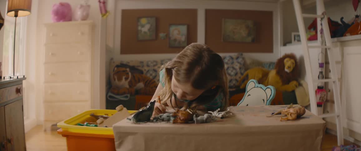 A young girl with a crayon in her hand leans over her table while coloring