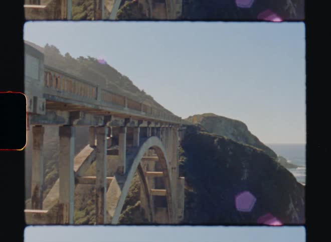 A bridge is build across a chasm in the mountains that line a coastal area Big Sur California Super8 4k Film Scan