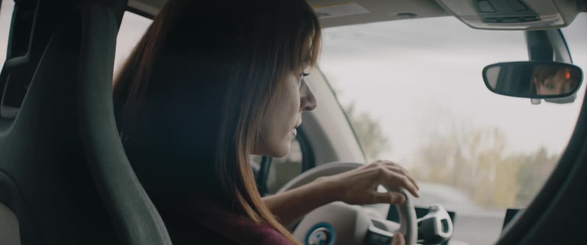 Woman with brown hair and maroon shirt drives car on highway