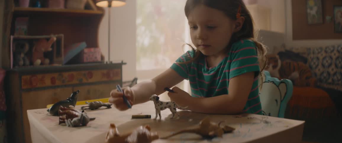 A little girl is sitting at her desk coloring with crayons