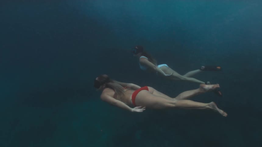 Two women in bikinis swimming underwater and kicking to the surface
