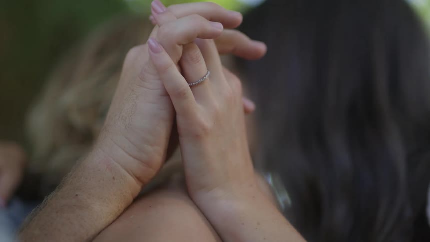 A man and woman holding hands and kissing while in a hammock