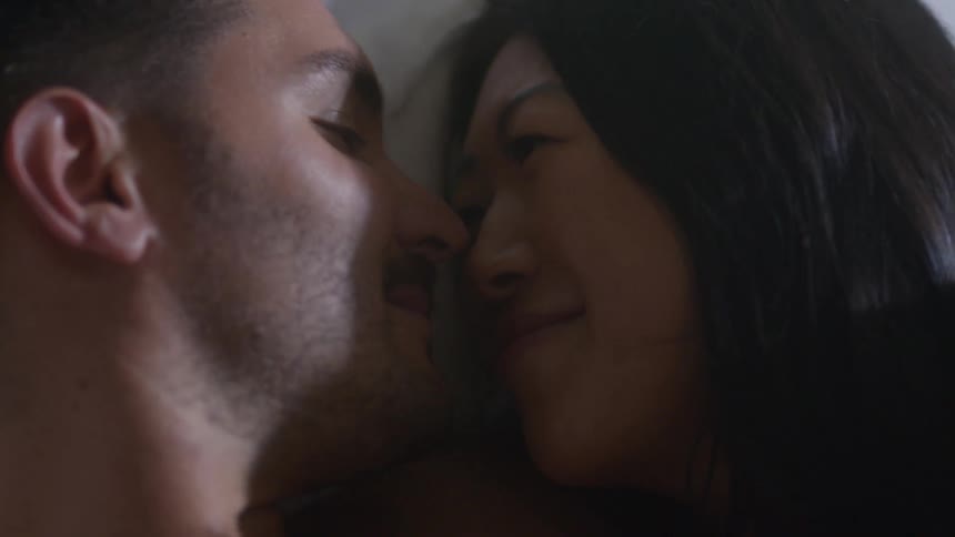 A man and woman lying in bed face to face smiling and cuddling