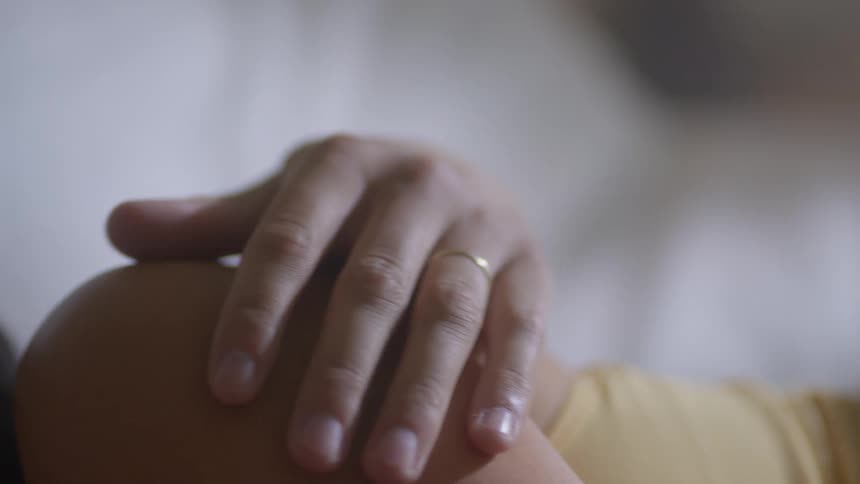 A woman caresses another womans shoulder as they lie in bed