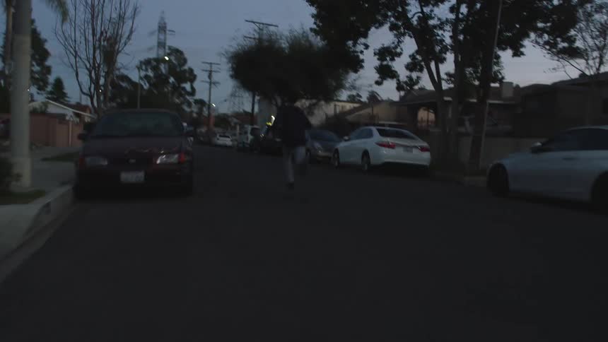 Teenaged boy opens the door of his house and runs down the middle of the street past the parked cars