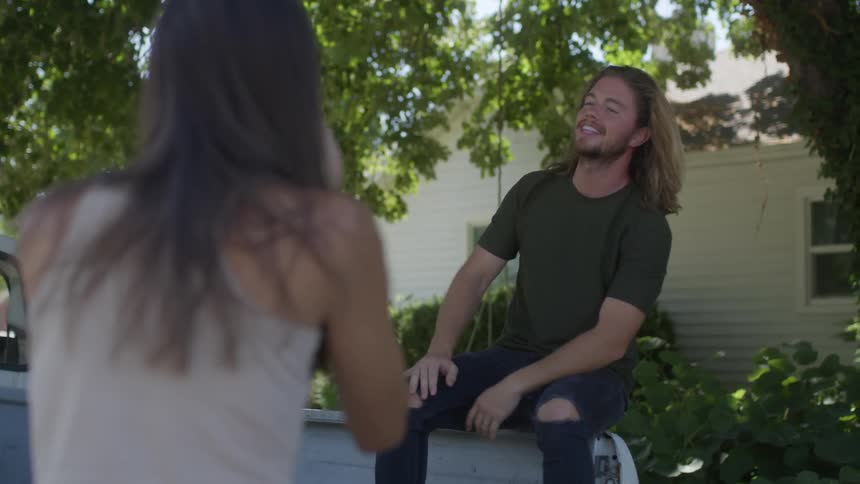 Man fluffs up his hair before tossing it back and posing on back of truck as woman takes pictures