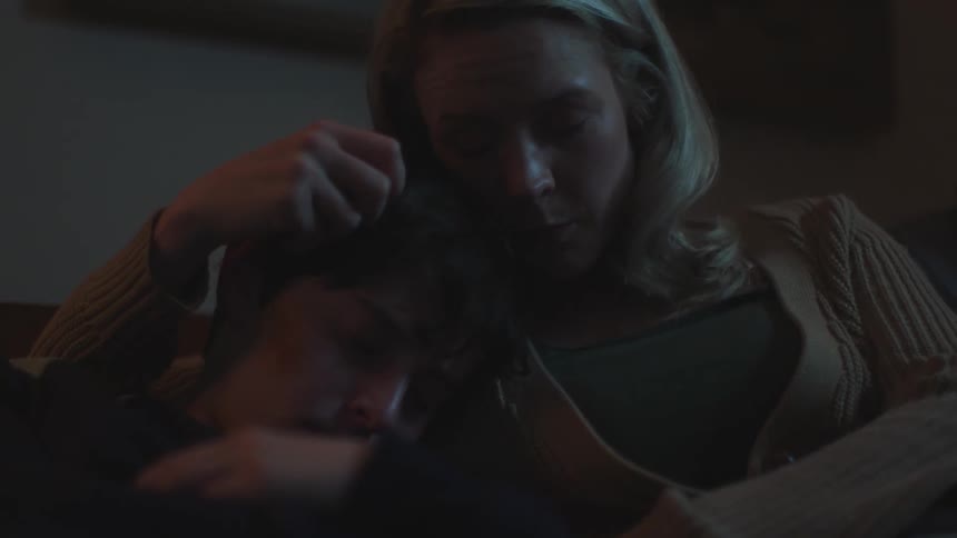 Mother cuddles sleeping son kissing and stroking his hair