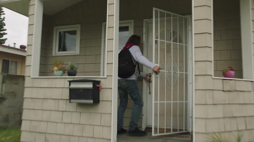 A man runs from his car in the driveway up the steps and into the house