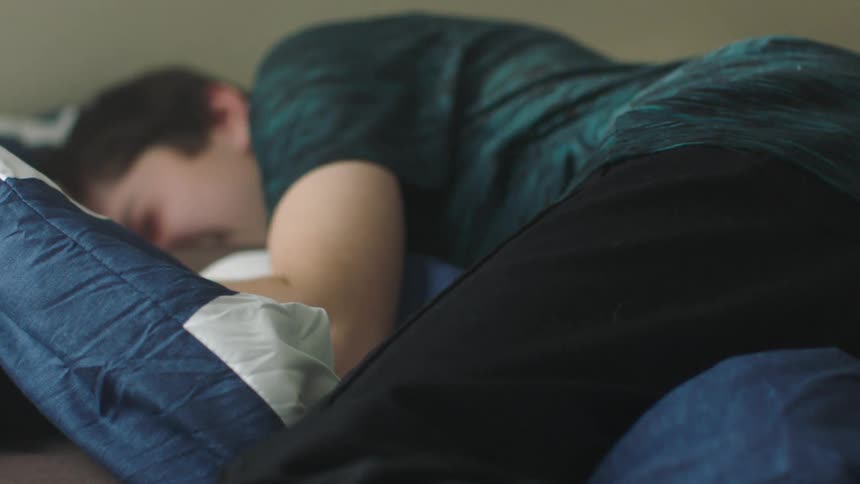 A boy jumps onto his bed and cries into his pillow