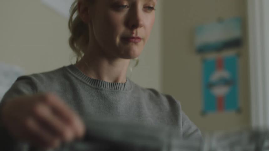 A woman buttons and folds a shirt in her bedroom