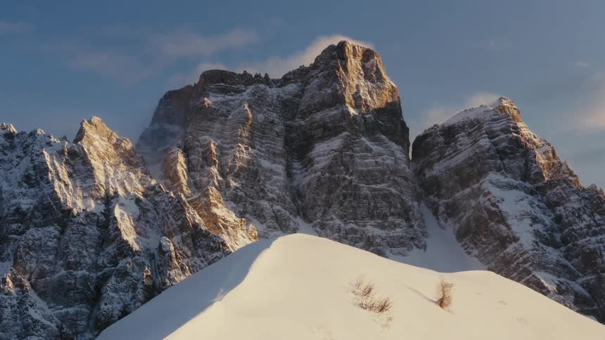 Leafless tree tops peak through snow on slope near towering mountains
