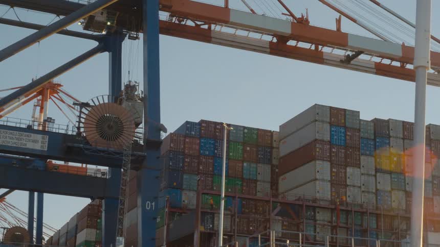 A crane lifts and moves a shipping container into position to stack on a cargo ship