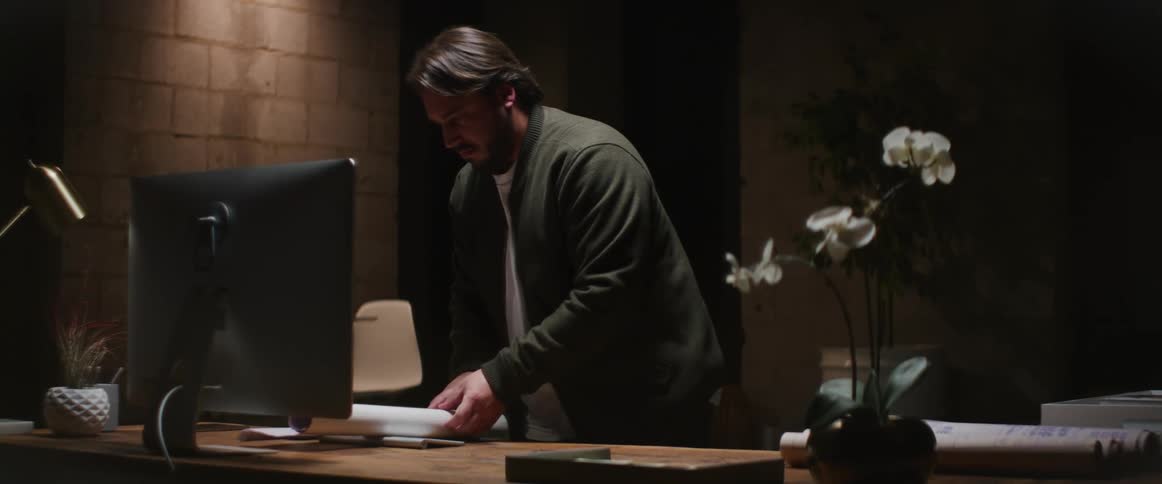 A man rolls up blueprints while standing at his desk