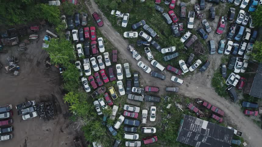 Cars in an auto salvage yard parked on grass and dirt roads