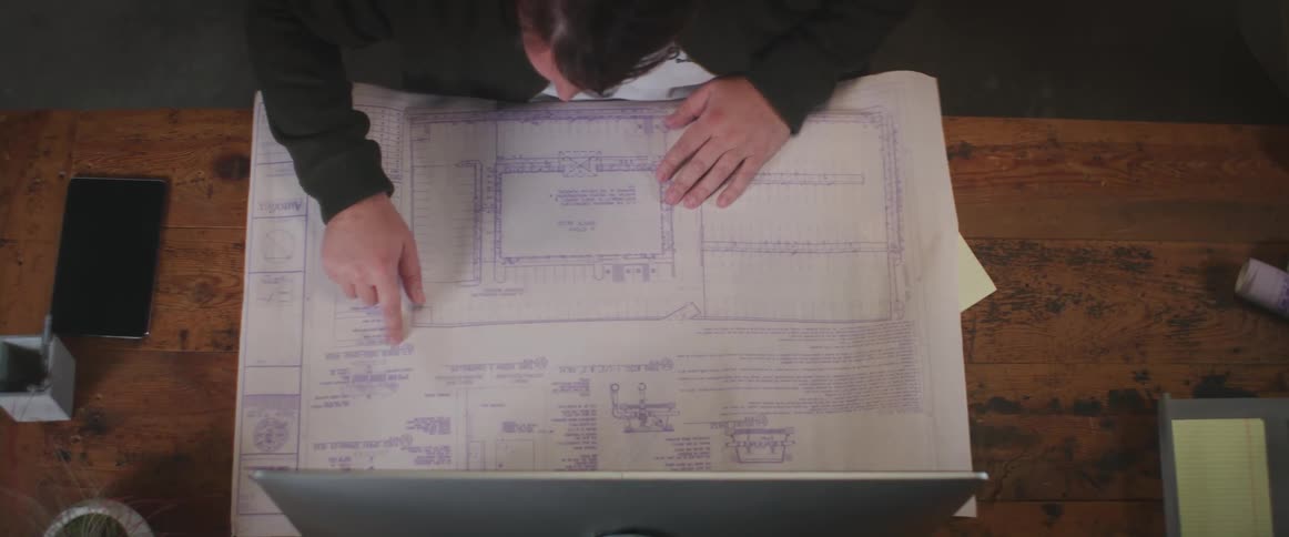 Man looks at a diagram and points his finger to a spot on the diagram then looks up at a monitor