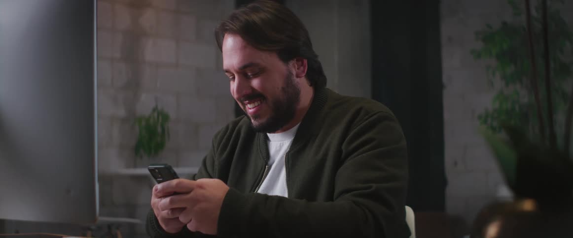 A man laughs while using his phone at the desk
