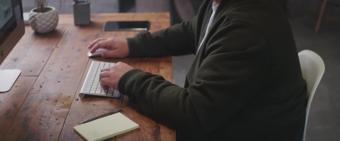 Man with green jacket and white shirt sits at desk and types on computer keyboard
