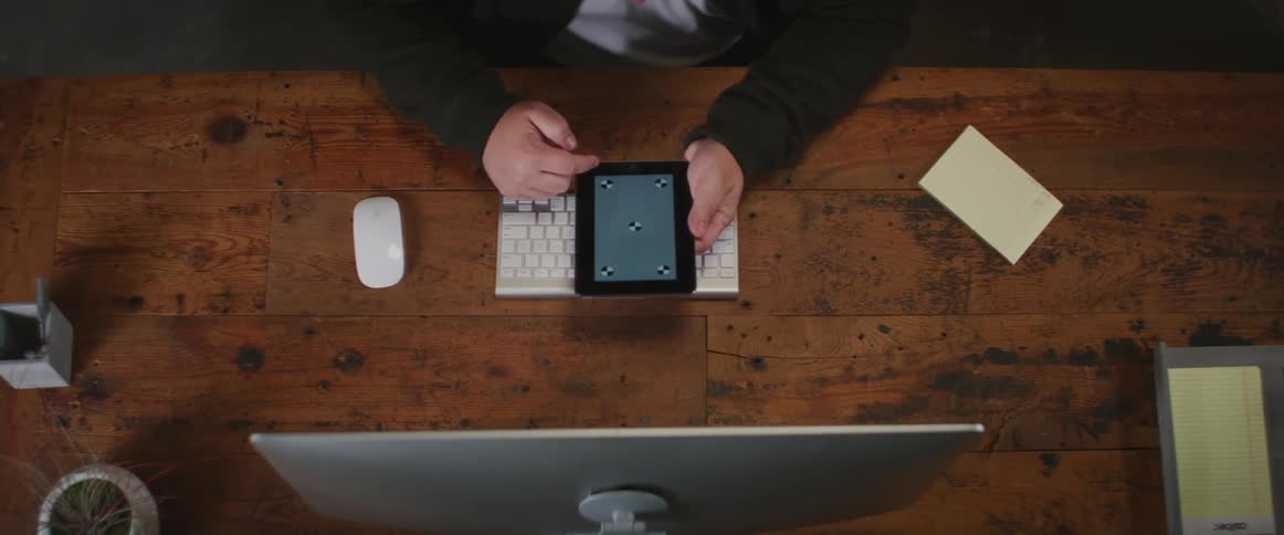 A man is sitting at a desk holding his phone and moving his finger across the gray screen with symbols