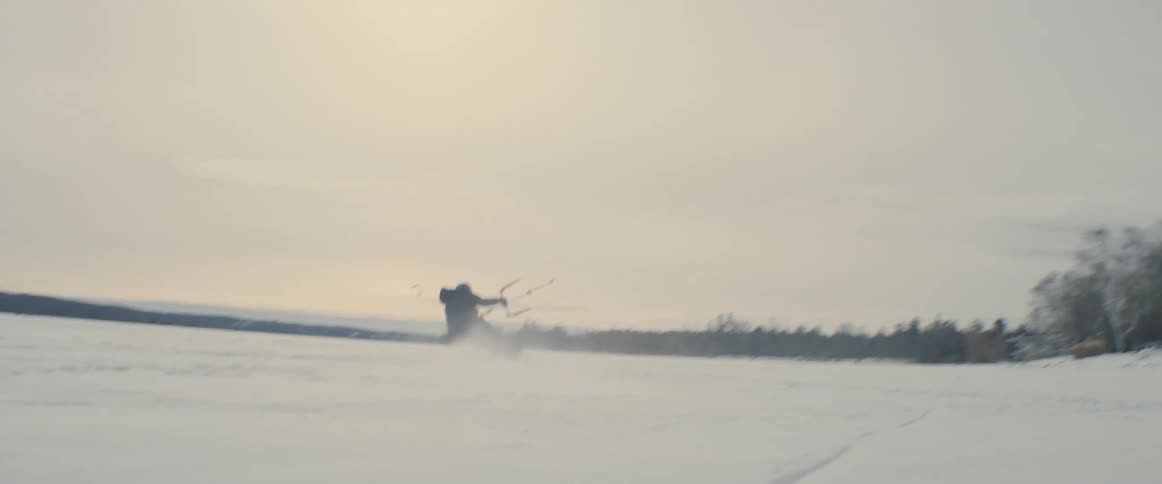 A man kite skiing over a snow covered frozen lake