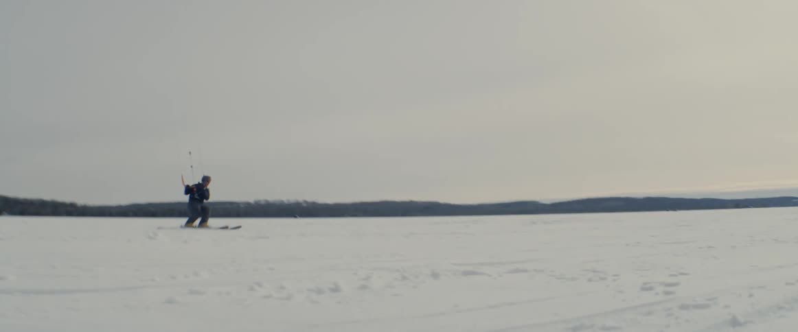 Skier holds on to a handlebar as he jumps in the air over the snowy field