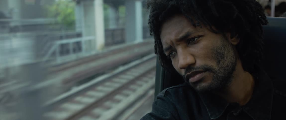 Man sits on a train as it travels on the tracks past some white pillars