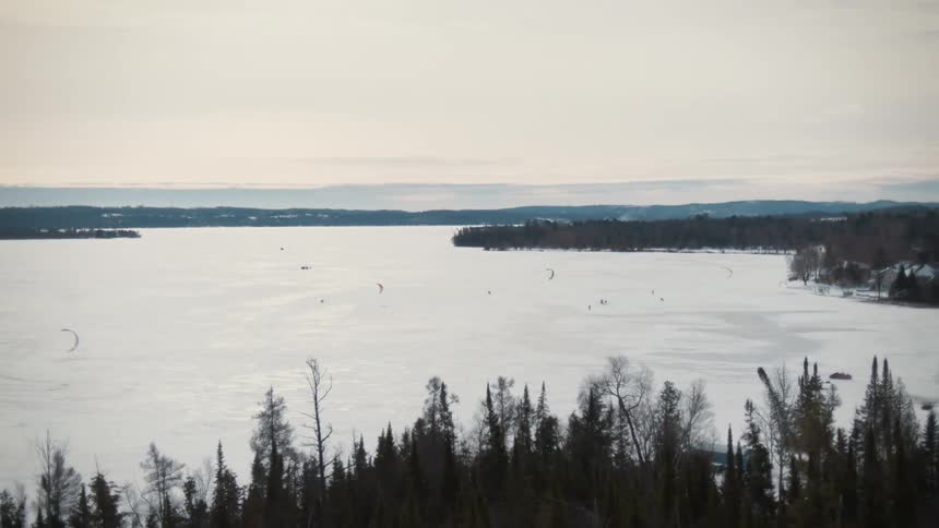 Aerial view of people skating over the frozen surface of a lake surrounded by pine tree forests