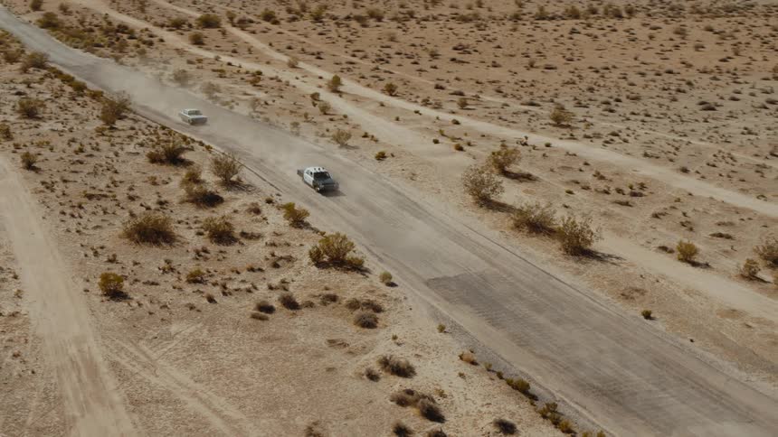 Two vintage police cars traveling on a desert road followed by a vintage sedan