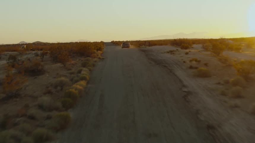 Aerial view of car driving on dirt road at sunset