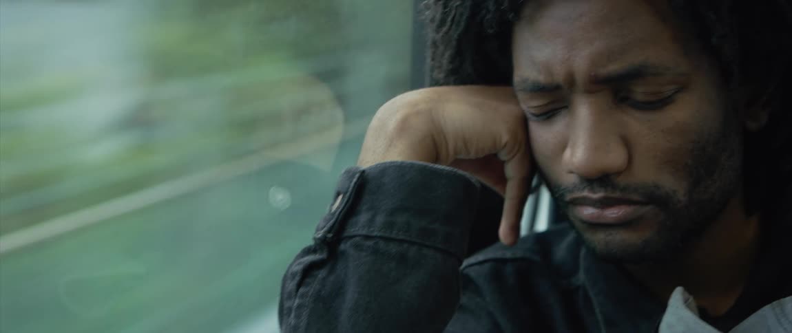Bored man sitting on a moving train with head reclined upon his hand looking out the window