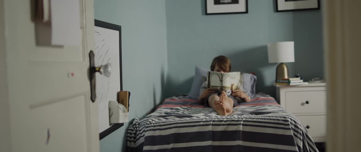 A girl is sitting up in her bed reading a book