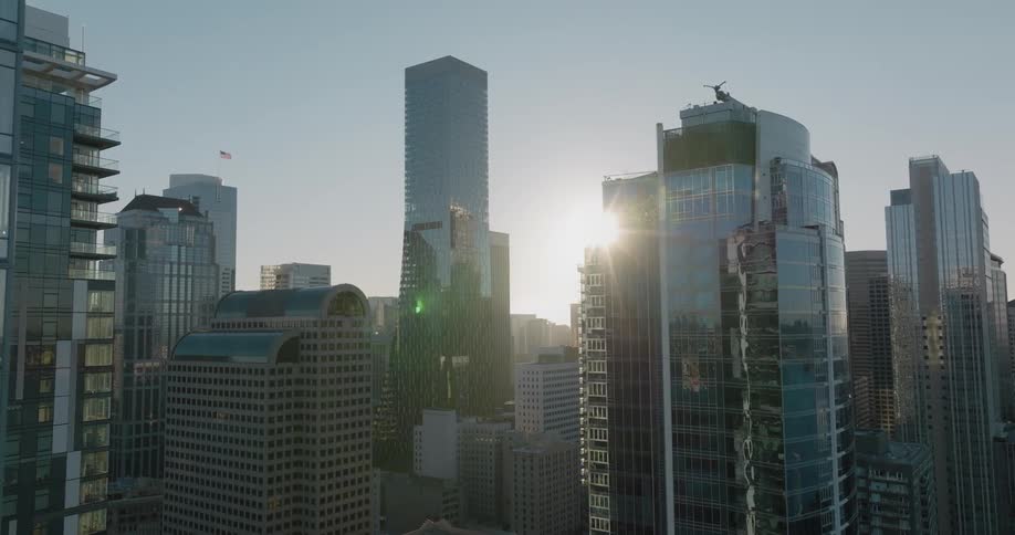 Reveal of the sun from behind tall buildings and skyscrapers under a clear morning sky